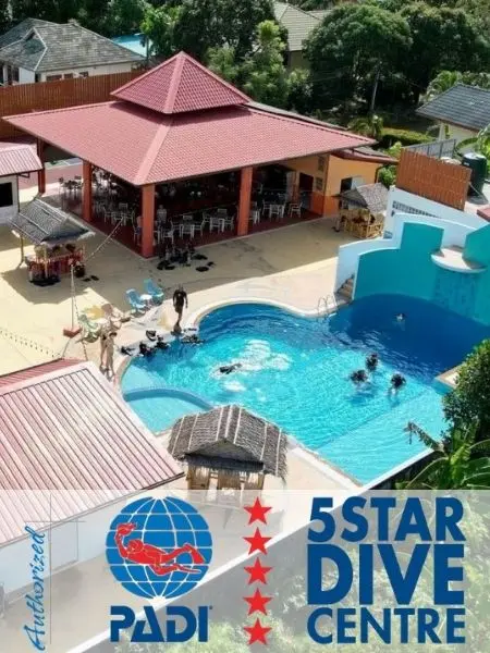 Flygfoto över ett PADI 5-stjärnigt dykcenter i Phuket, Thailand, med en träningspool, dykelever och en skuggig uteservering omgiven av tropisk grönska.