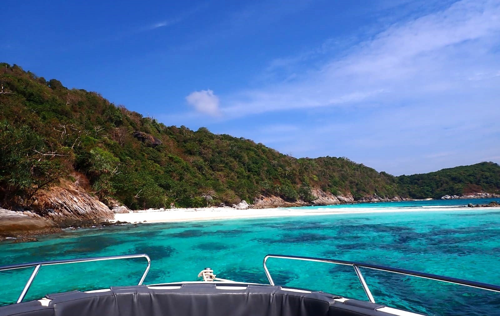 Turquoise Racha Noi Bay and its sandy beach seen from the bow of the private speedboat