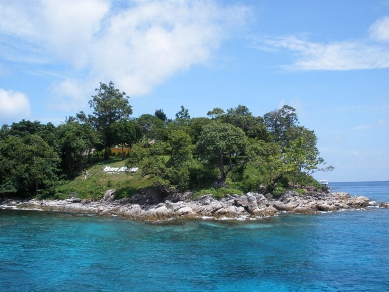 Granite shoreline and tropical trees beside clear water at Racha Yai