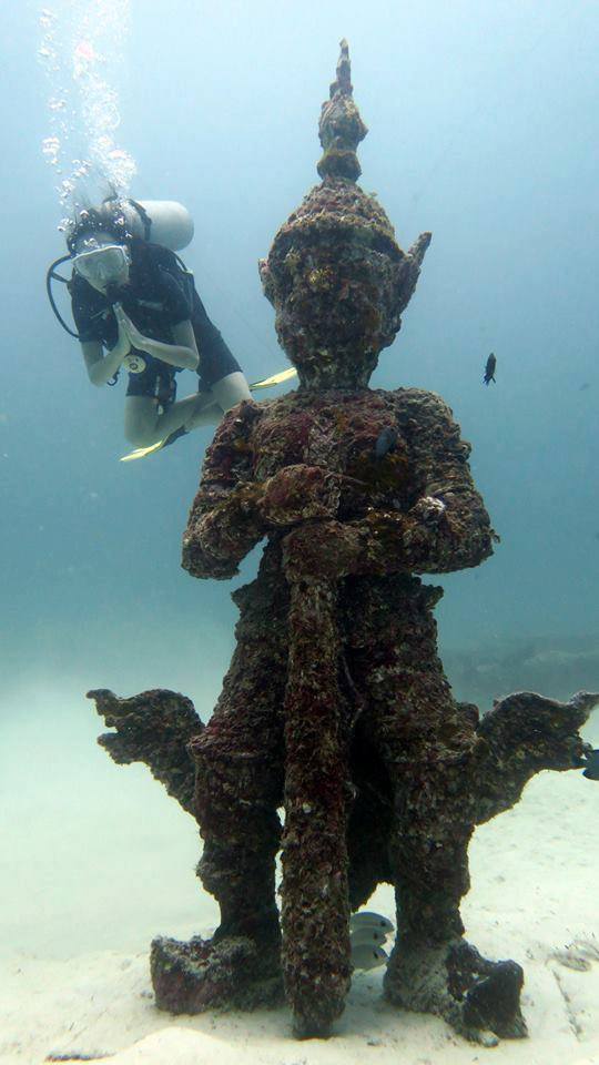 Scuba diver beside a coral-covered underwater Yak guardian at Racha Yai